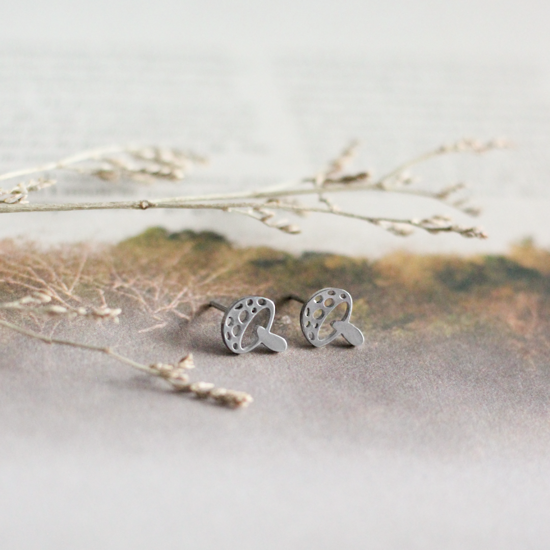 Silver earrings on a light background with dried leaves