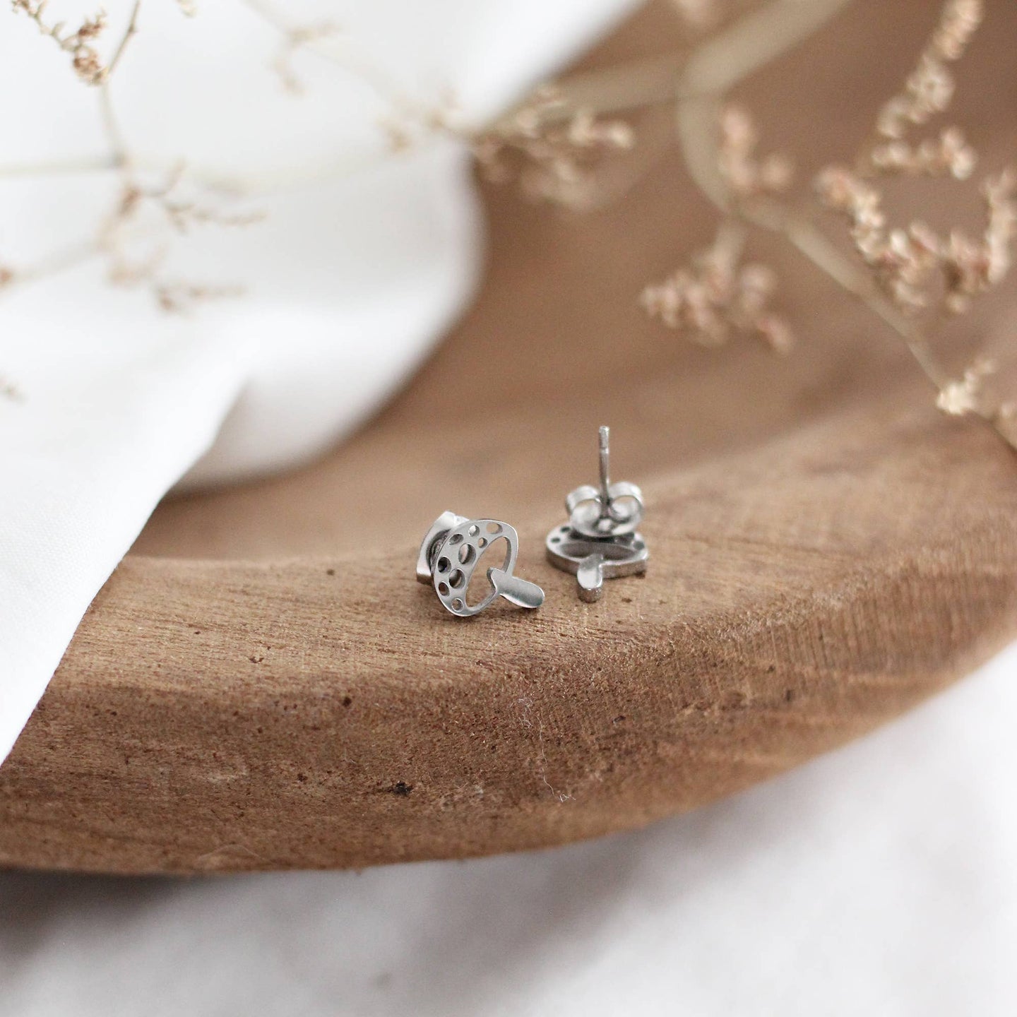 Silver mushroom shaped earrings on a wooden surface with a marble background
