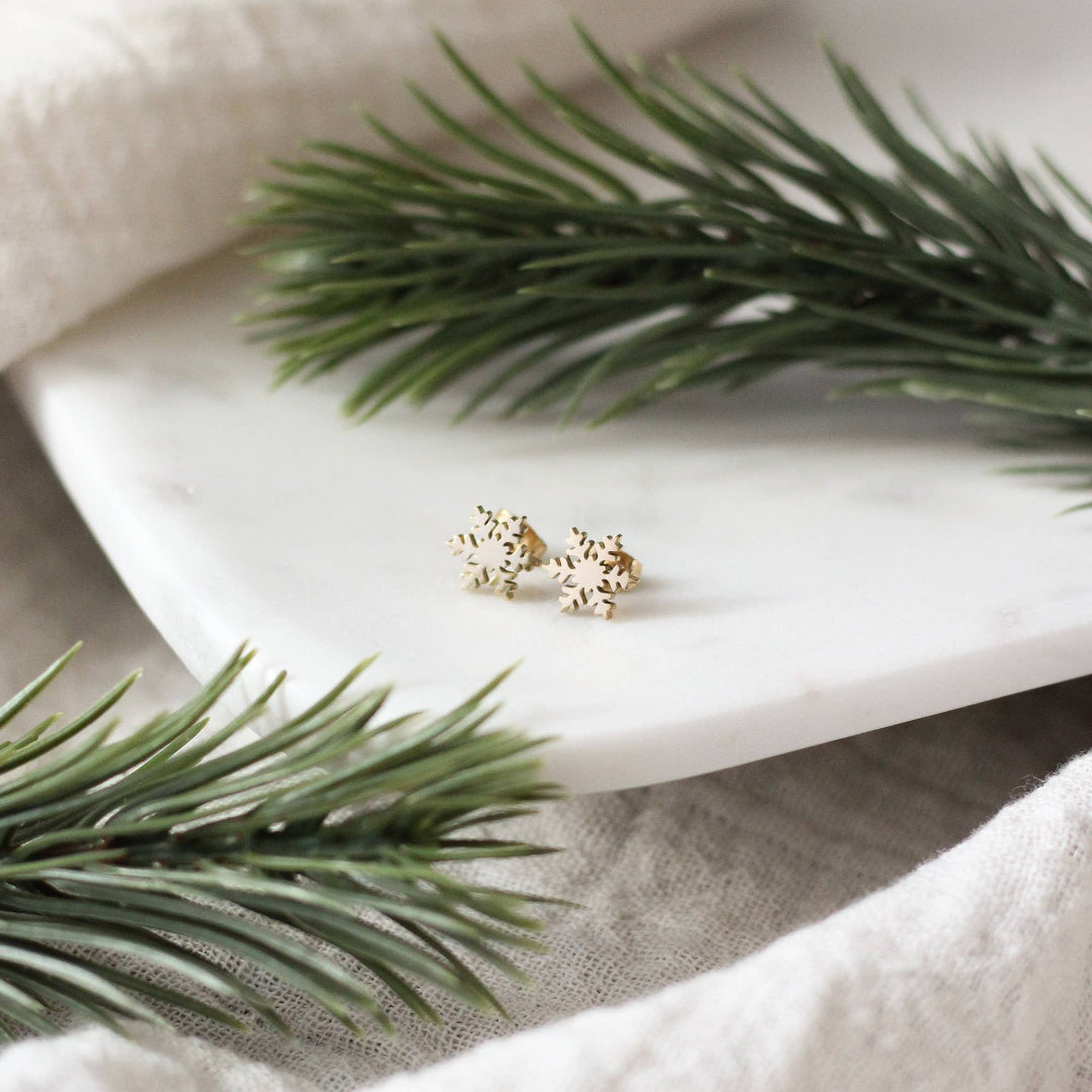 Gold earrings on a white marble surface with green leaves