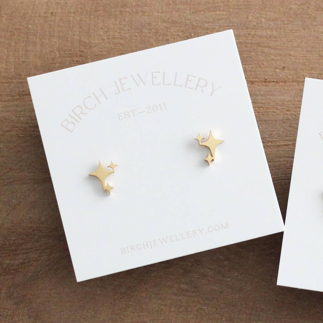 Two pairs of earrings on branded cards against a wooden background