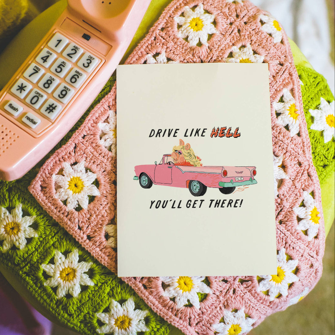 Notebook with 'Drive Like Hell, You'll Get There!' text on a pink phone and crocheted surface with flowers.