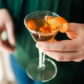 A glass jar filled with dried orange slices, cocoa nibs, and other ingredients. The jar has a white label with the Maiden Voyage logo and the product name "Mocha Old Fashioned Cocktail Infusion." 