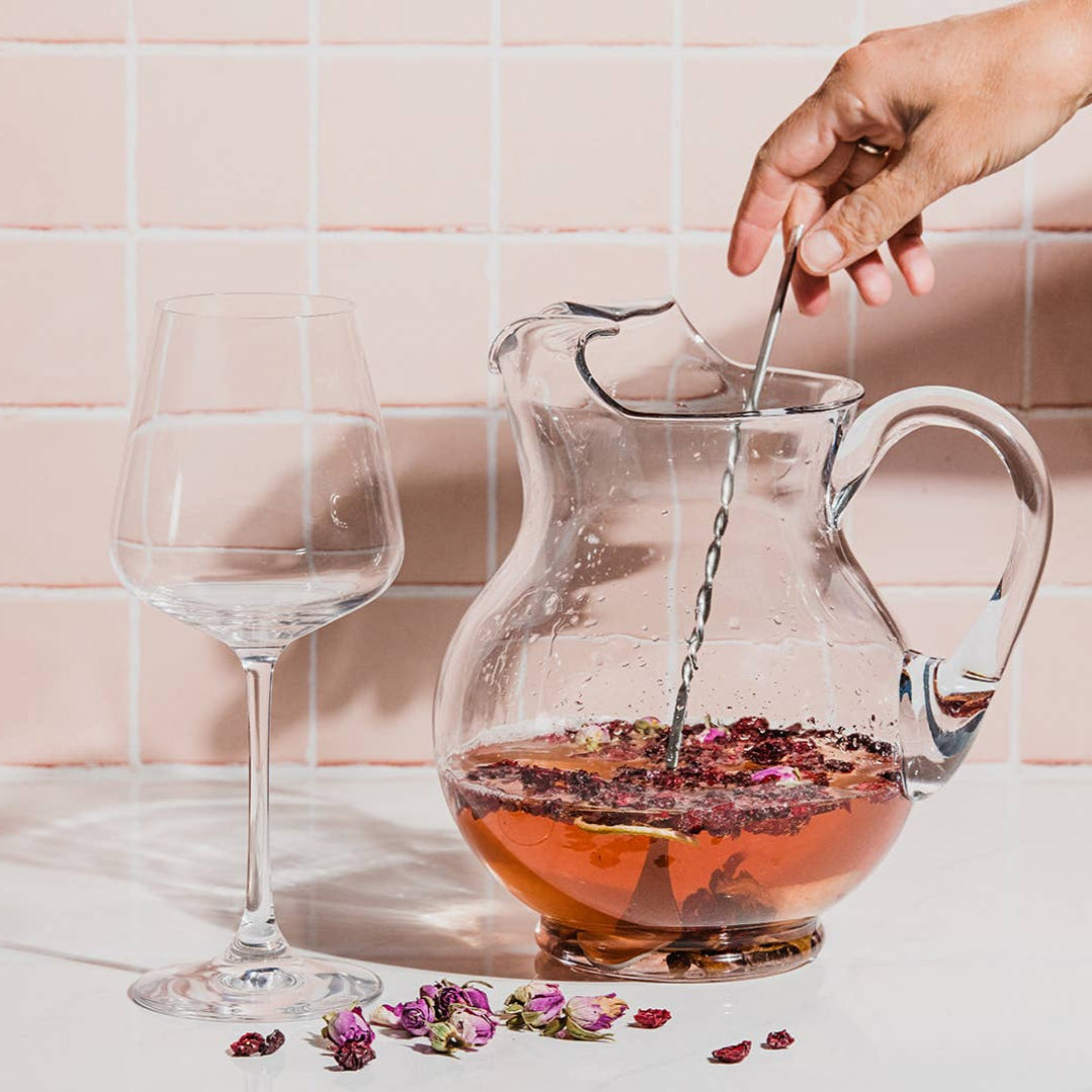Person pouring tea into a glass teapot with a pink tiled wall background