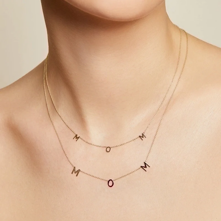 A delicate gold-filled necklace spelling out 'MOM' with individual letter charms evenly spaced along a fine chain, displayed on a white background. This heartfelt necklace is available in Ottawa, Ontario, Canada.