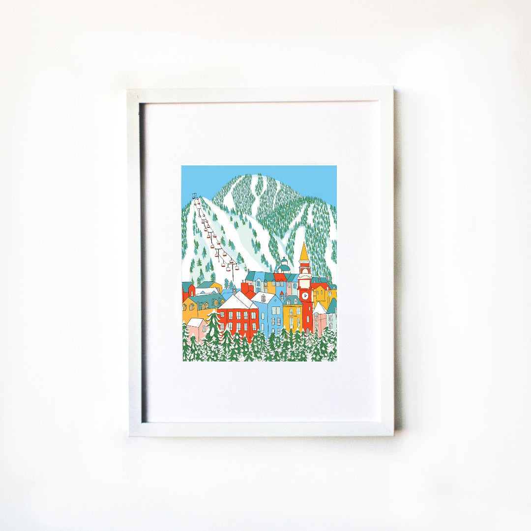 Framed artwork of a colorful mountain village scene on a white wall