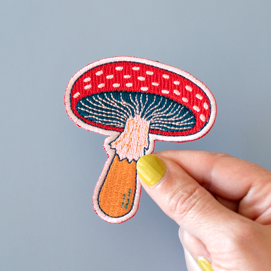Hand holding a embroidered mushroom patch against a gray background