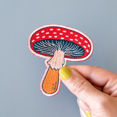 Hand holding a embroidered mushroom patch against a gray background