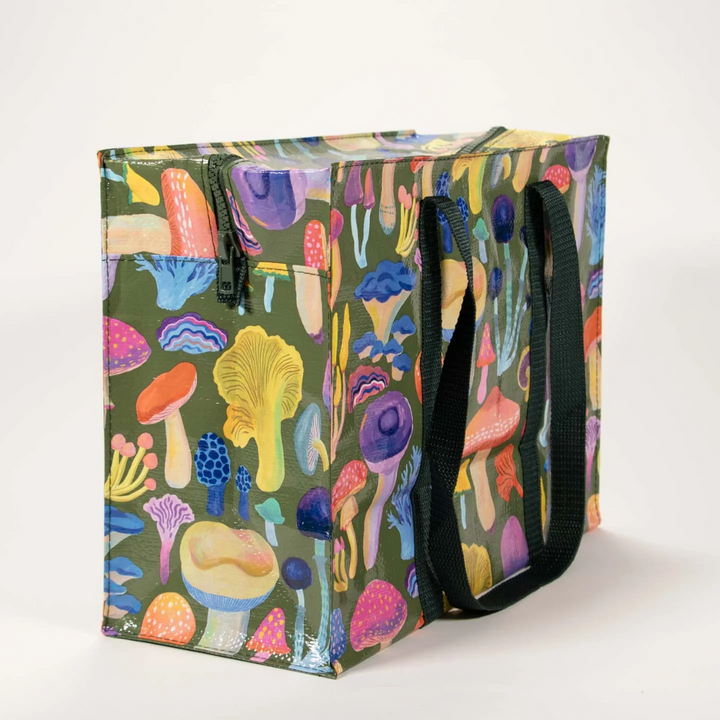A large, reusable tote bag with a mushroom pattern. The bag is olive green with black handles. It is covered in a variety of colorful mushrooms in different shapes and sizes.