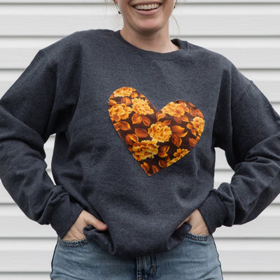 Person wearing a dark gray sweatshirt with a floral heart design, standing against a light-colored wall.