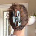 Person with a light blue hair clip in their brown hair, standing indoors.