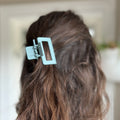 Person with wavy hair wearing a light blue hair clip against a blurred background