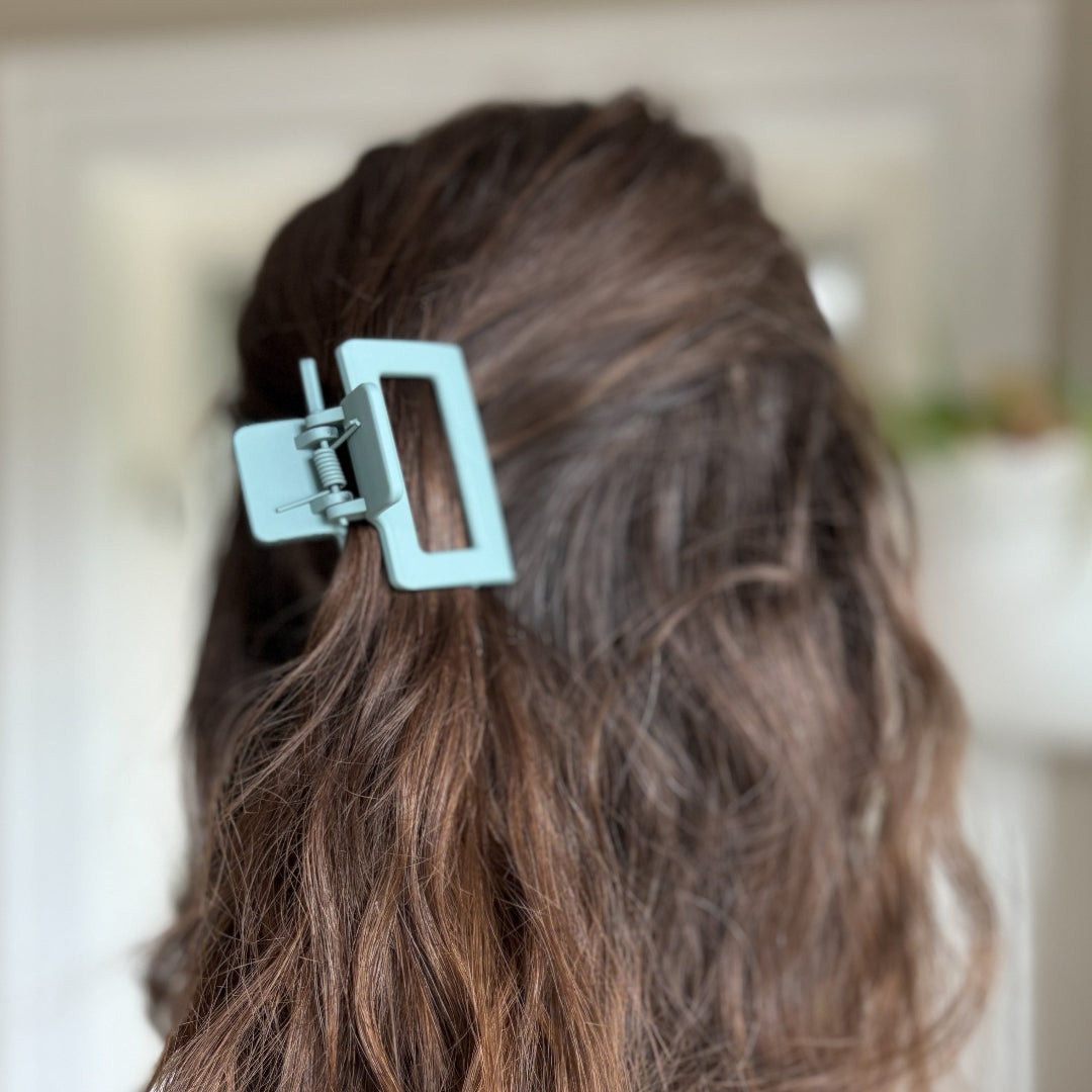 Person with wavy hair wearing a light blue hair clip against a blurred background