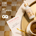 A styled flat-lay featuring a white cosmetic bottle with a gold dropper cap labeled 'MY CAFE' on a gold tray, alongside a cup of coffee, a guest check pad, and promotional text for CBC Dragons' Den, OTB Morning Live, and GQ.