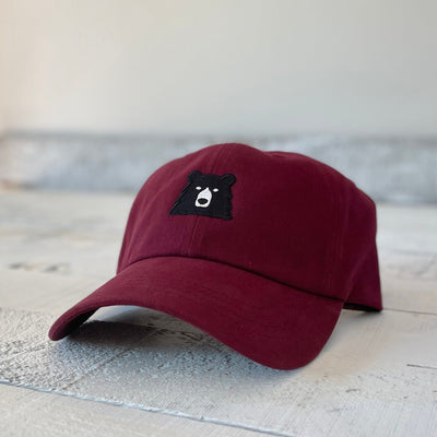 Maroon cap with a bear face emblem on a wooden surface