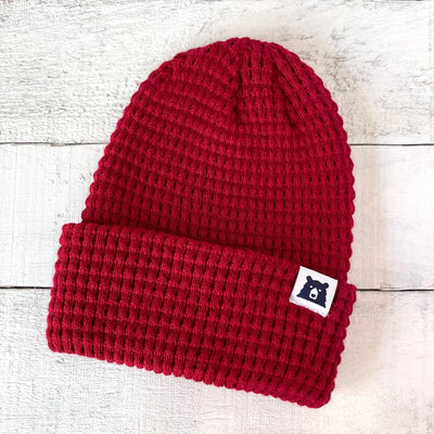 Red knit beanie with a small logo on a light wooden surface