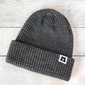 Gray knit beanie with a logo patch on a light wooden background