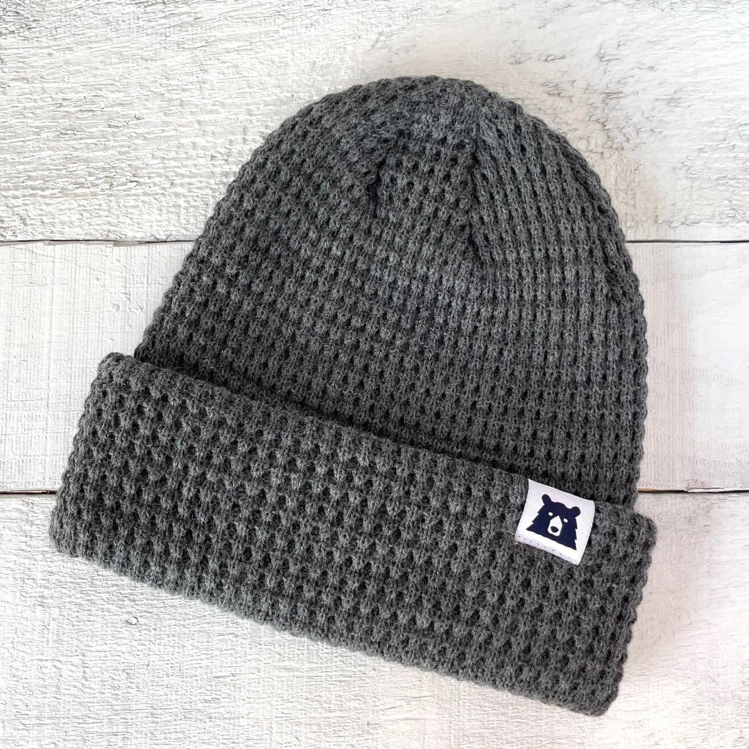 Gray knit beanie with a logo patch on a light wooden background