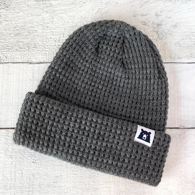 Gray knit beanie with a logo patch on a light wooden background