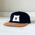 Navy blue cap with brown visor and white bear logo on a light gray surface