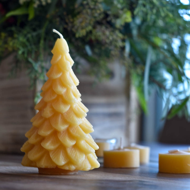 A yellow, beeswax candle shaped like a Christmas tree. The candle has detailed branches and a pointed top.