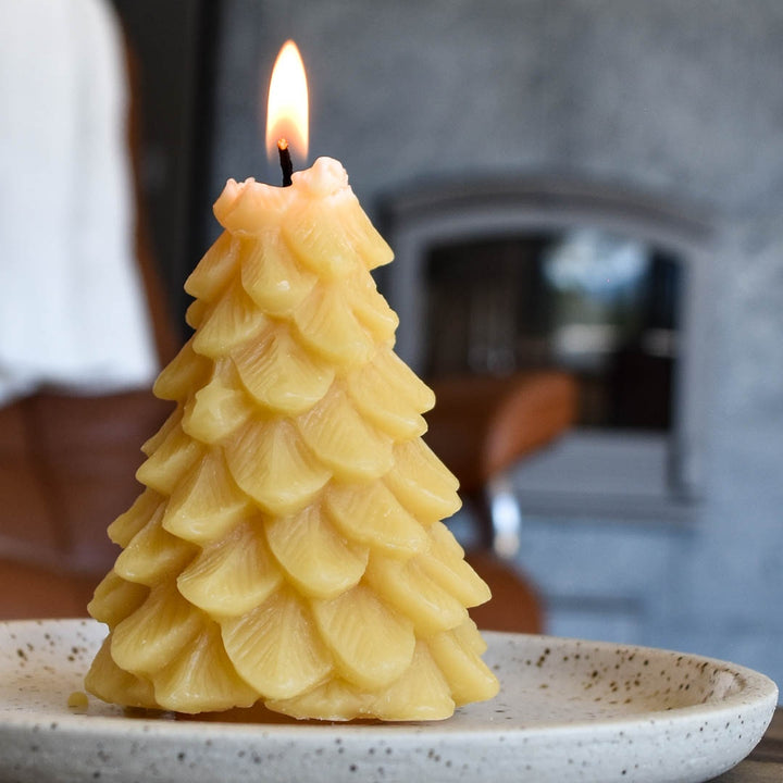 A yellow, beeswax candle shaped like a Christmas tree. The candle has detailed branches and a pointed top.
