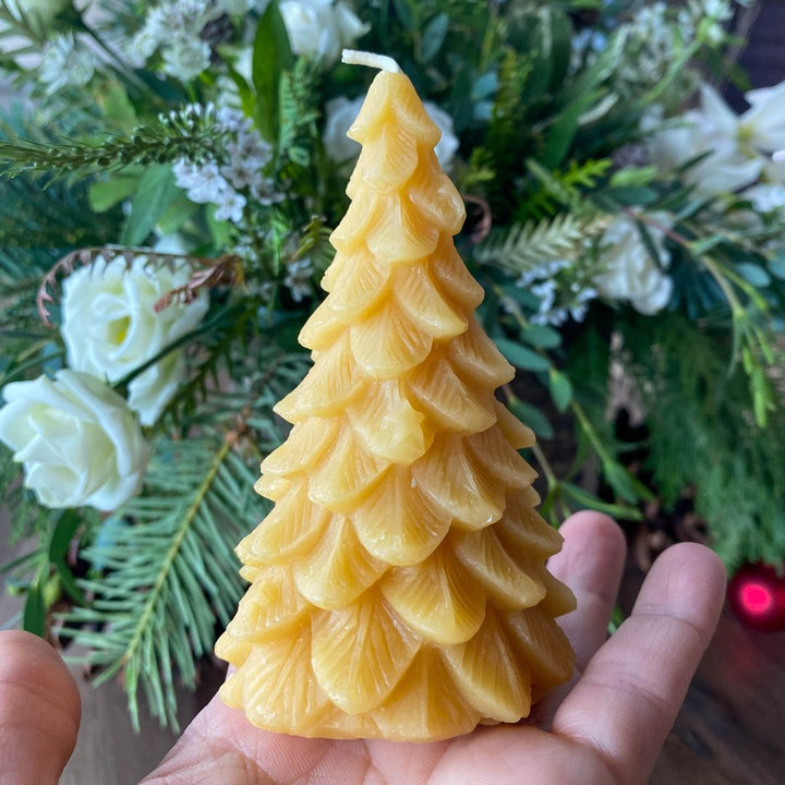 A yellow, beeswax candle shaped like a Christmas tree. The candle has detailed branches and a pointed top.