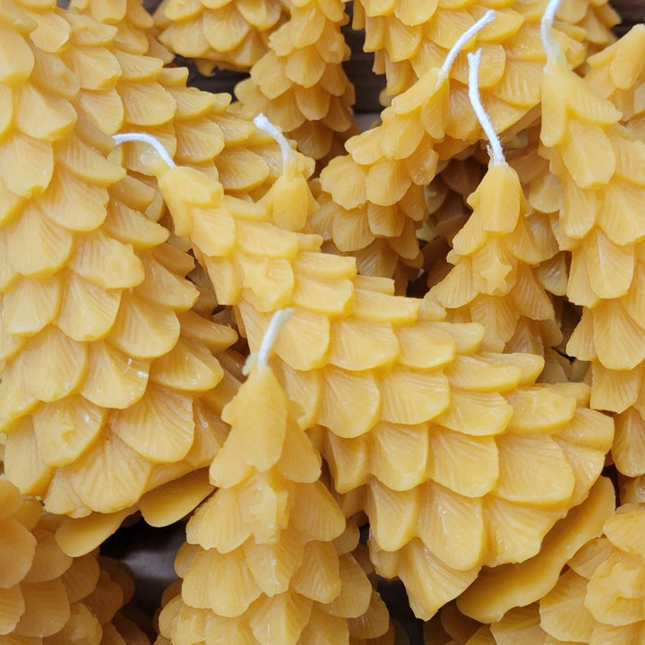 A yellow, beeswax candle shaped like a Christmas tree. The candle has detailed branches and a pointed top.
