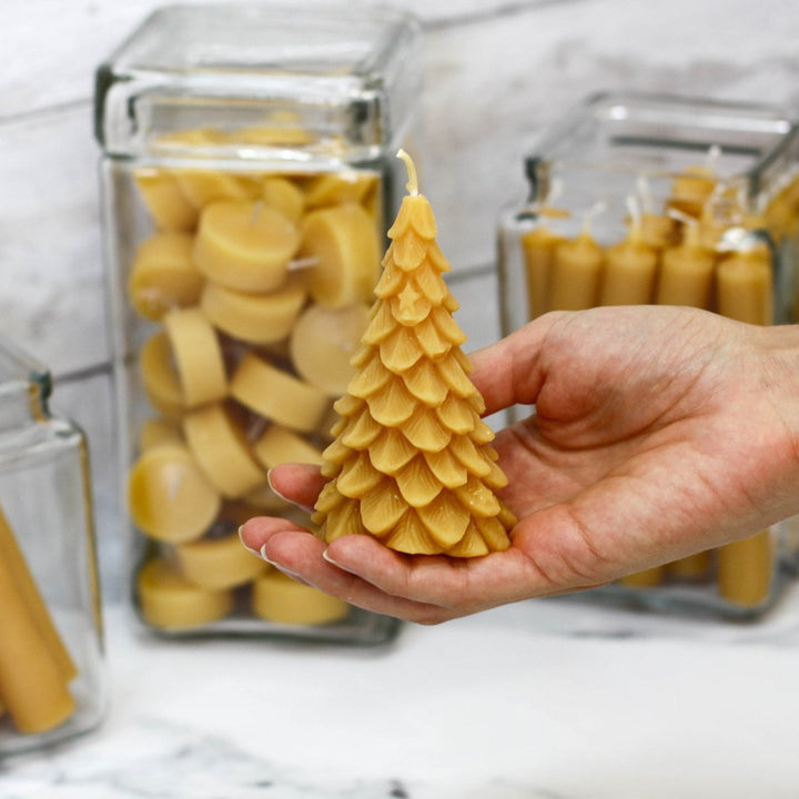 A yellow, beeswax candle shaped like a Christmas tree. The candle has detailed branches and a pointed top.