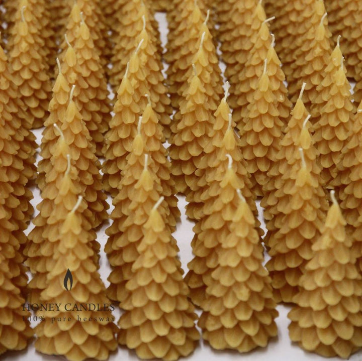 A yellow, beeswax candle shaped like a Christmas tree. The candle has detailed branches and a pointed top.