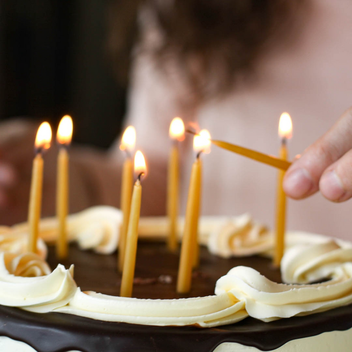A chocolate cake with white frosting and yellow beeswax candles lit on top.