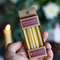 A hand holding a small cardboard box of birthday candles. The box contains 10 yellow beeswax birthday candles and has a label that says 