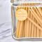 A close-up of a glass jar filled with thin, yellow beeswax candles. The jar has a label that says 