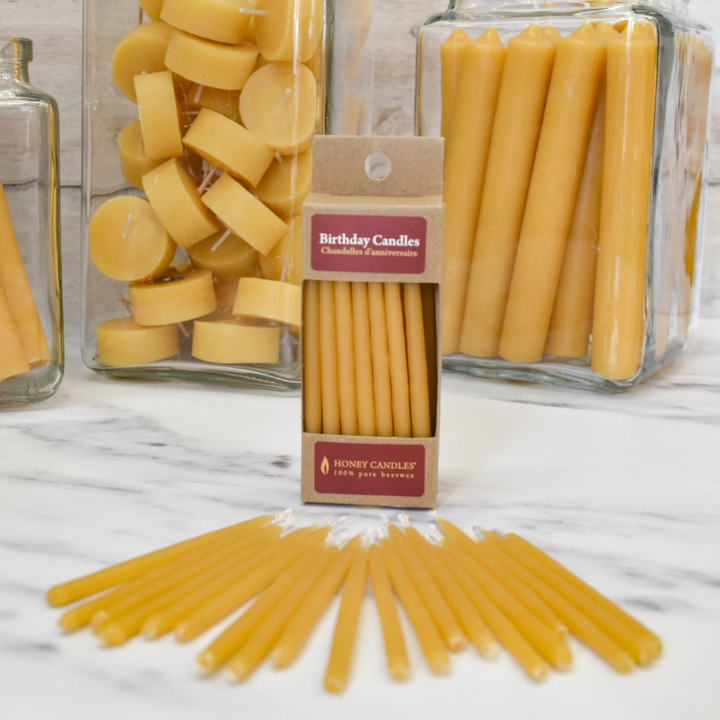 A cardboard box of birthday candles on a white marble surface. The box contains 10 yellow beeswax birthday candles and has a label that says 