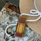 A cardboard box of birthday candles resting on a green canvas bag with a floral pattern. The box is tied to a white rope and there is a straw hat and a bracelet nearby.