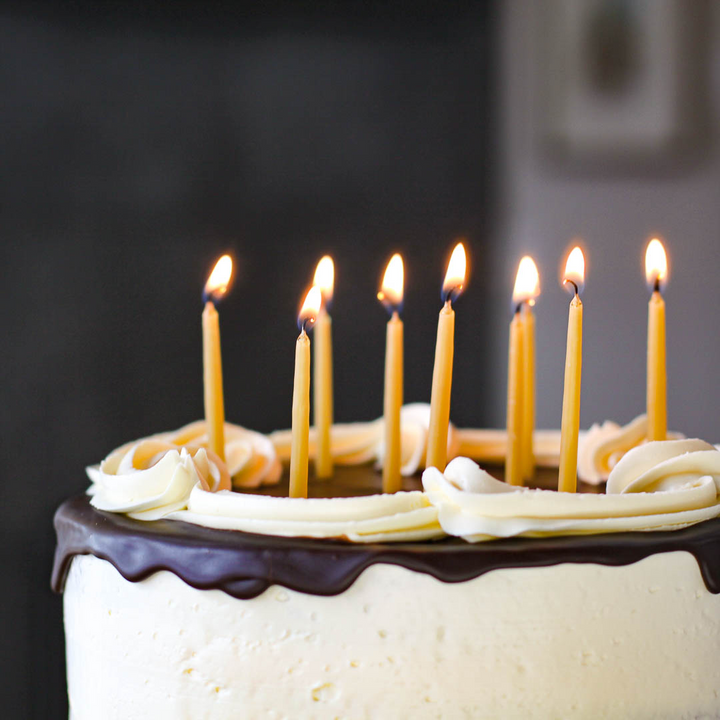 A chocolate cake with white frosting and yellow beeswax candles lit on top.