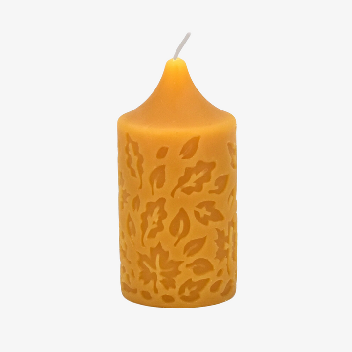 A yellow beeswax pillar candle with a leaf pattern.