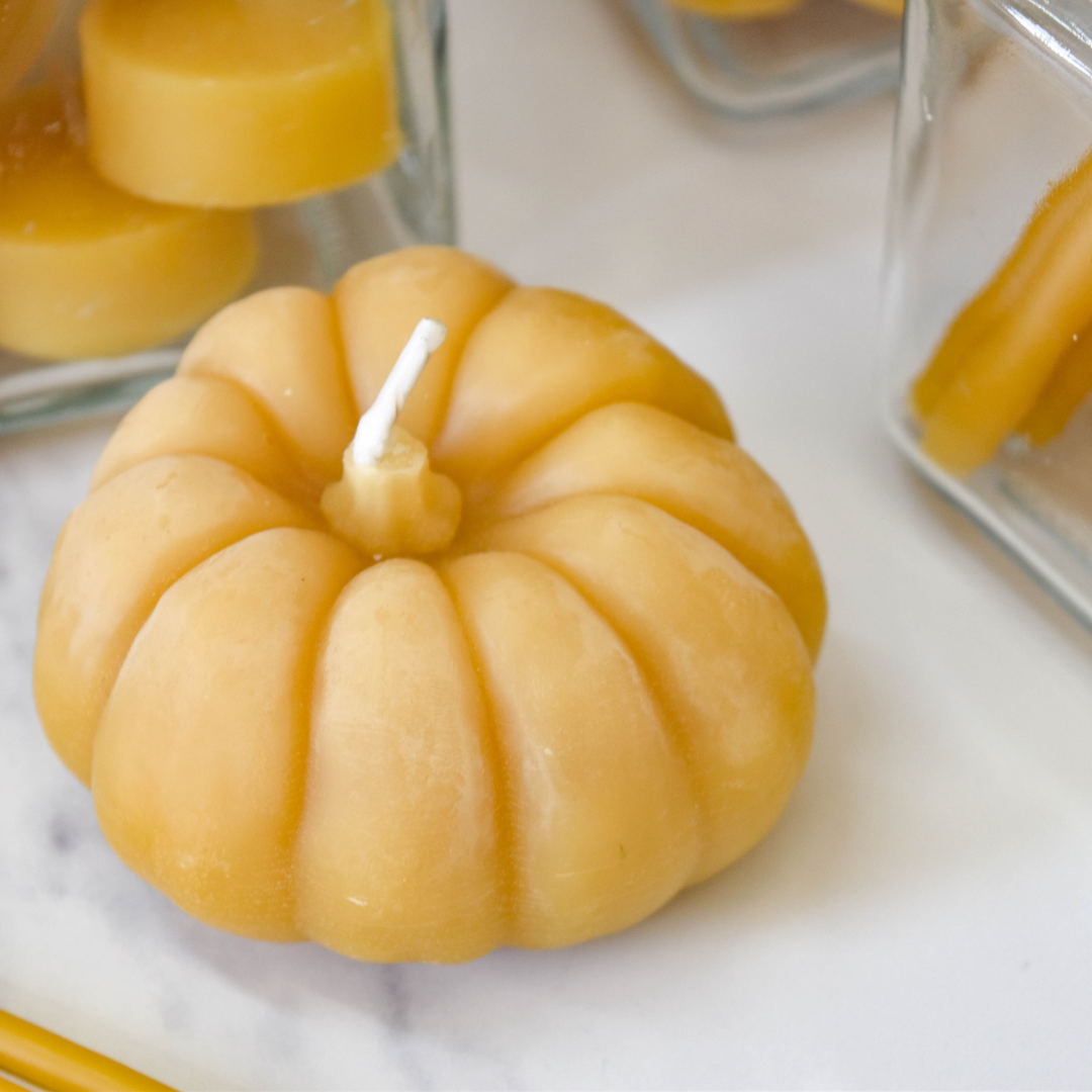A small, pumpkin-shaped beeswax candle. The candle is orange with detailed ridges and a wick in the center.