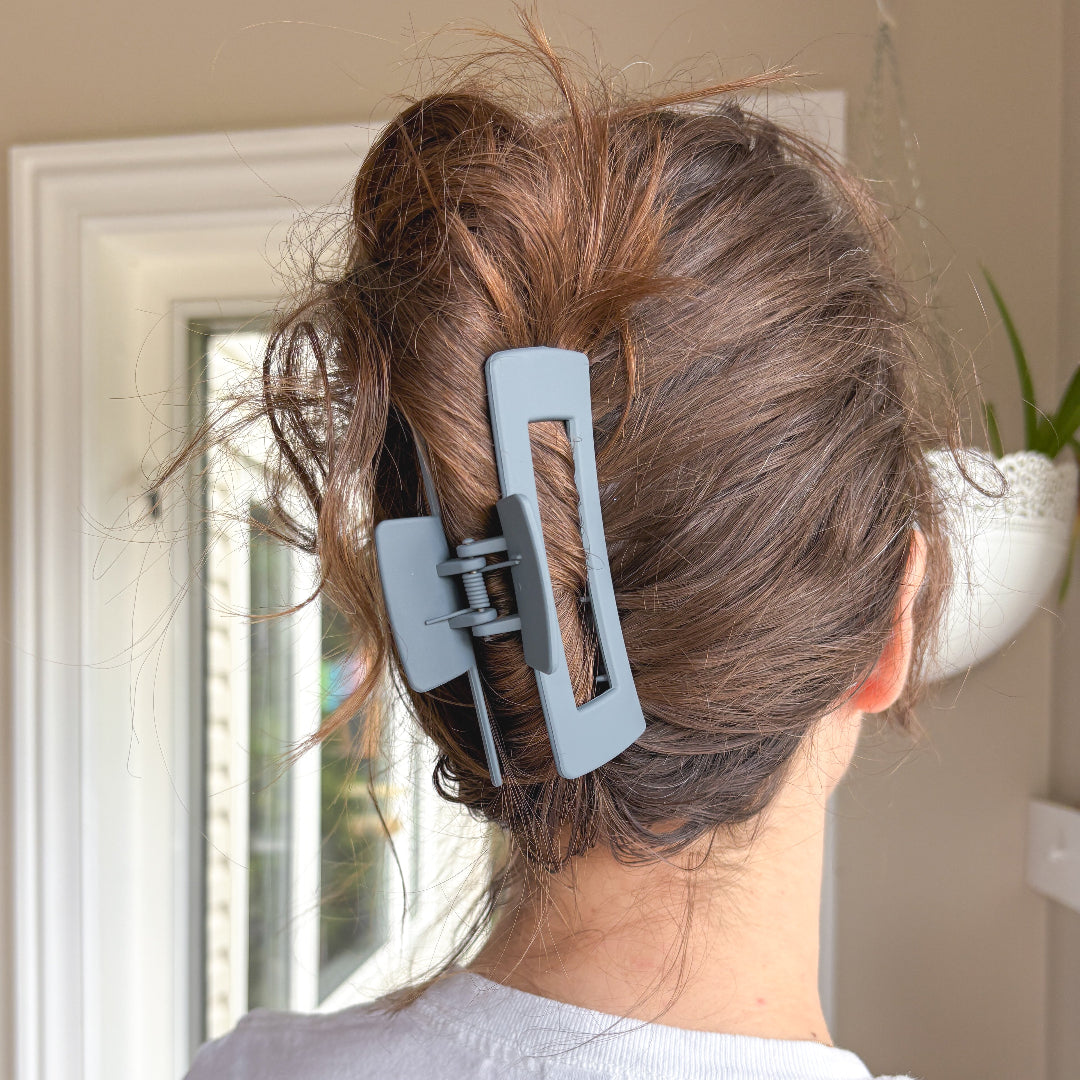Person with a blue hair clip in their hair, standing in a room with a window and plant.