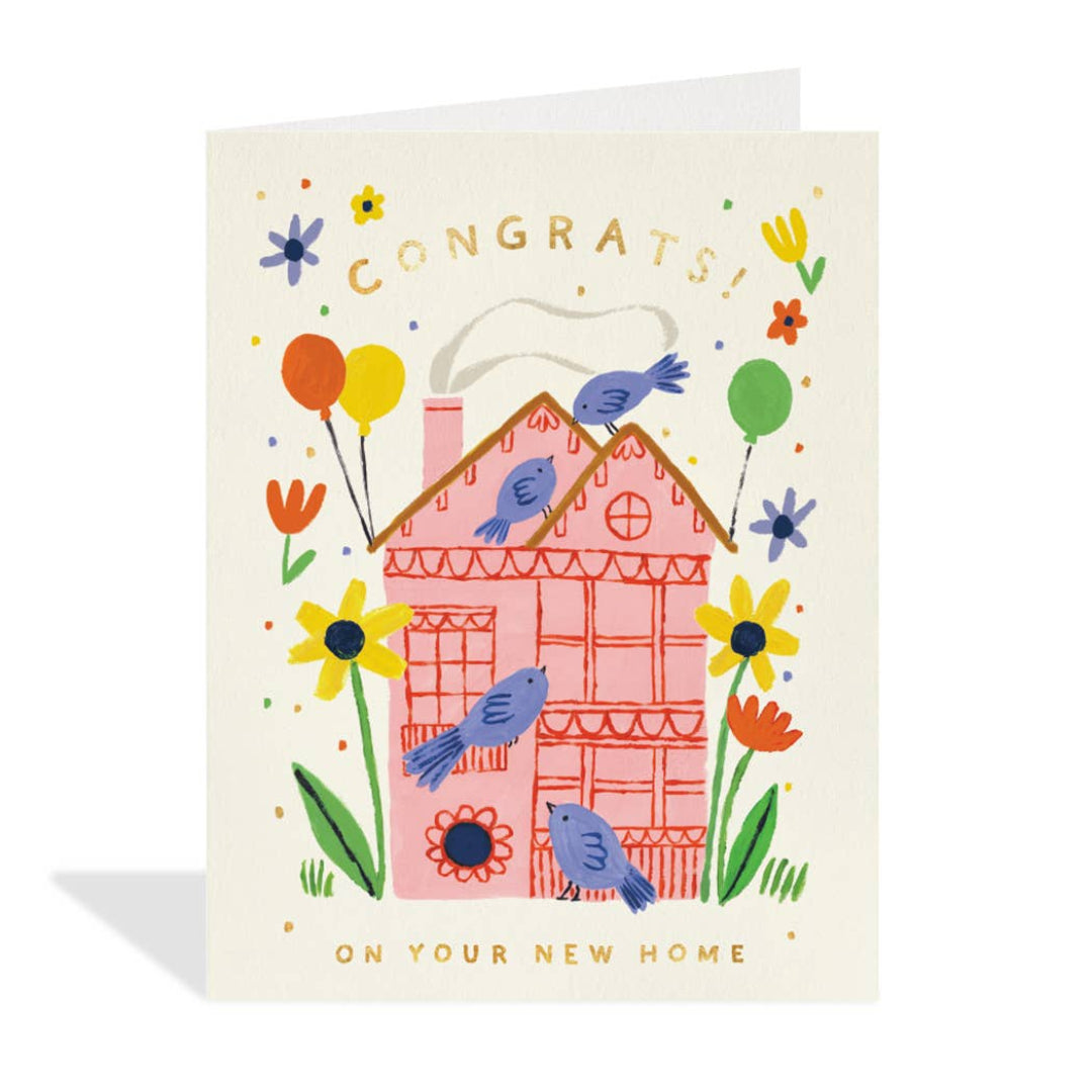 A rectangular greeting card with a cream background, featuring a whimsical illustration of a pink house surrounded by blue birds, yellow and orange flowers, balloons, and the words 'CONGRATS!' and 'ON YOUR NEW HOME'.