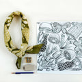 Green patterned headscarf, coloring book with mushroom design, and coloring supplies on a white background