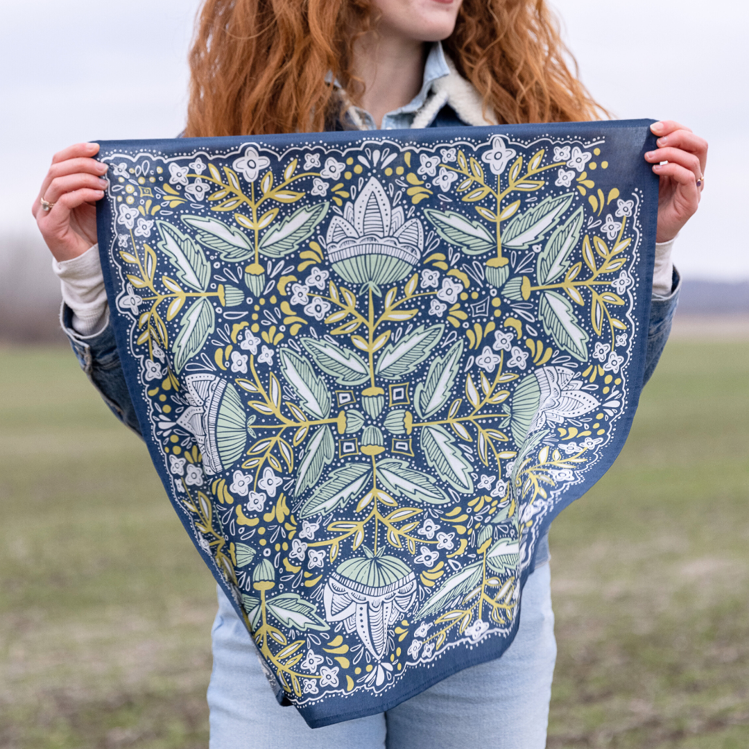 A navy blue bandana with a floral pattern in shades of green and yellow. The pattern features stylized flowers, leaves, and small dots.