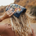 A navy blue bandana with a floral pattern. The pattern features stylized flowers, leaves, and berries in shades of yellow, orange, and pink.