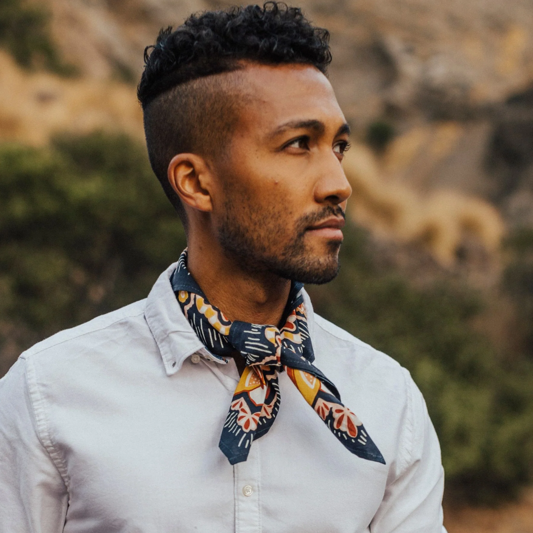 A navy blue bandana with a floral pattern. The pattern features stylized flowers, leaves, and berries in shades of yellow, orange, and pink.
