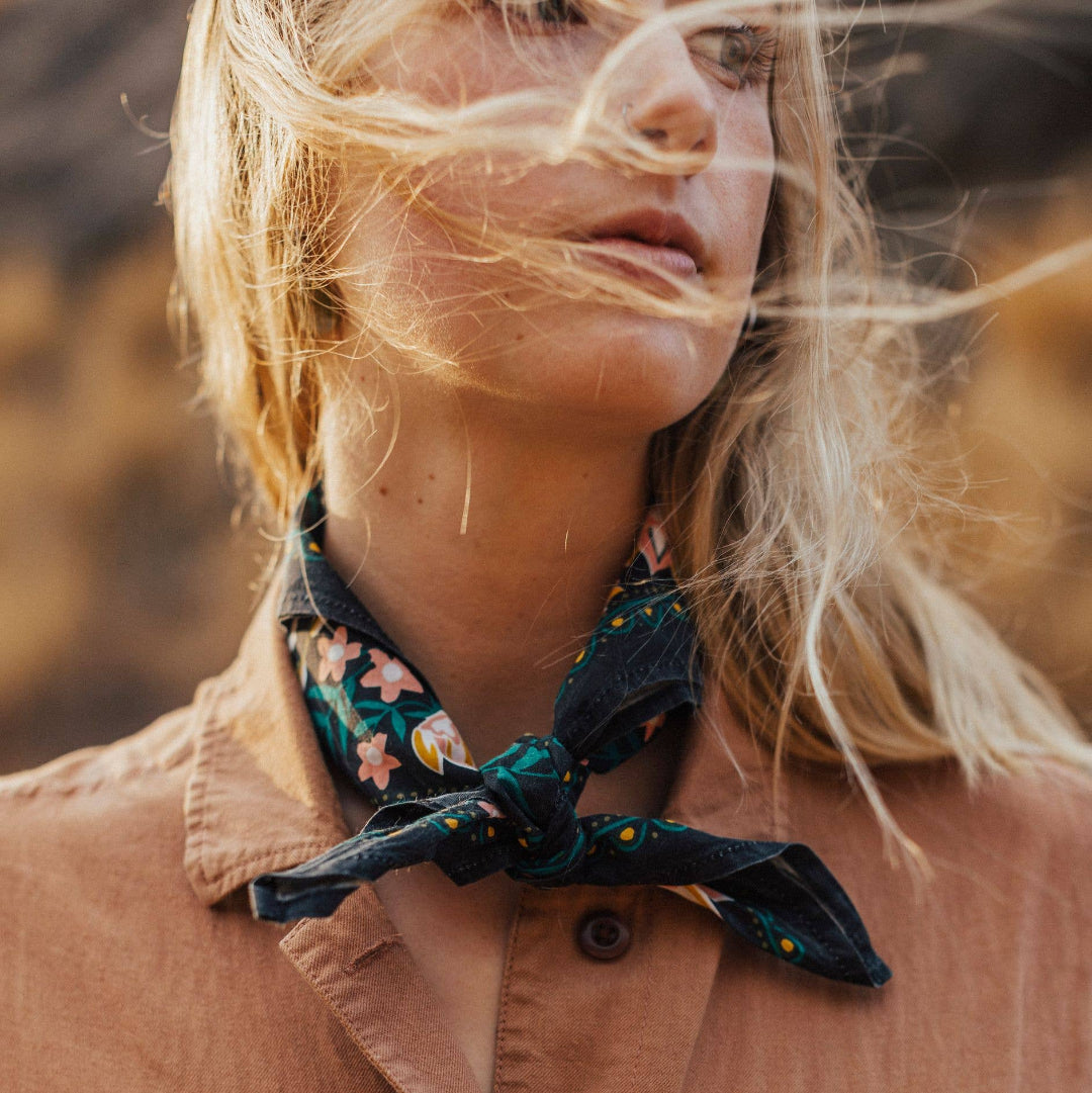 Person wearing a brown jacket with a floral scarf around their neck, outdoors.