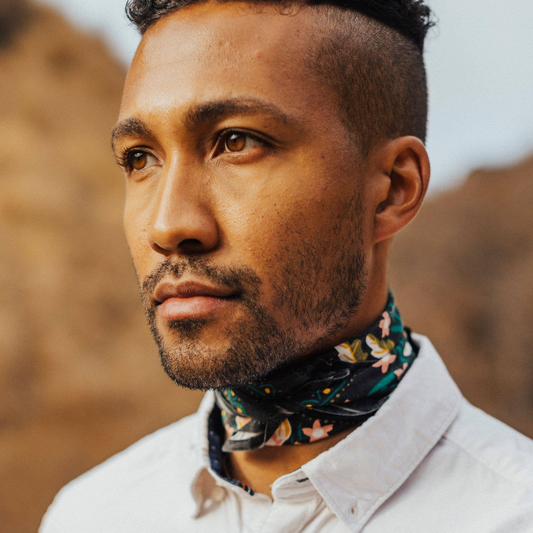 Man wearing a white shirt and floral neck scarf with a blurred natural background