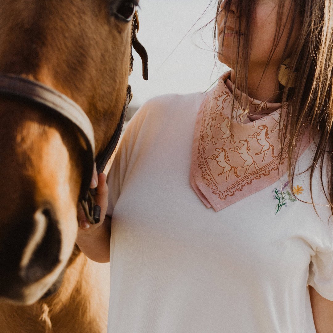 A pink bandana with a pattern of white galloping horses. The horses are evenly spaced and face in various directions.