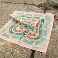 Decorative handkerchief with green and orange patterns on a concrete surface