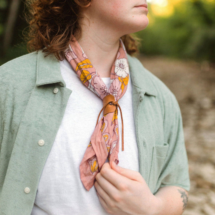 A pink bandana with a floral pattern. The pattern features white flowers with yellow centers and green leaves.