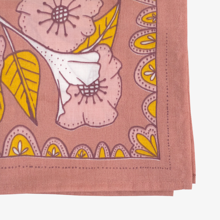 A pink bandana with a floral pattern. The pattern features white flowers with yellow centers and green leaves.