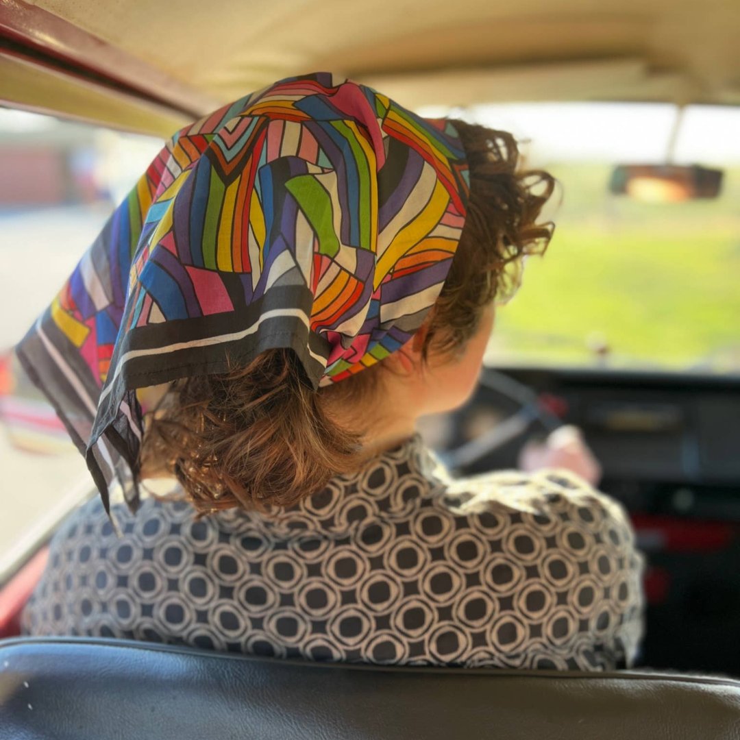 A black bandana featuring a pattern of overlapping Pride flags in various colors and designs. The flags include the classic rainbow flag, the transgender flag, and the bisexual flag.